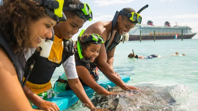 Família de snorkel observa uma arraia em água rasa, com o navio ao fundo